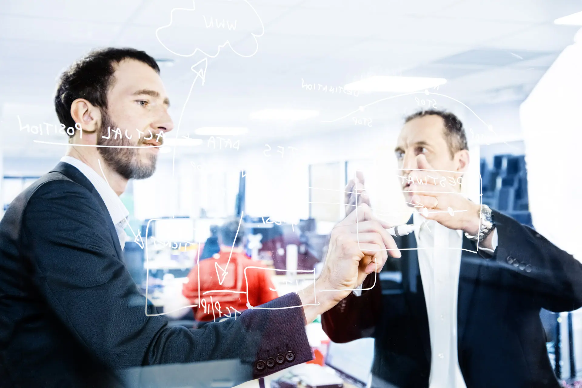 Zwei Männer skizzieren ein Konzept auf einer Glaswand. Unternehmensfotografie, Brainstorming, Ideenfindung.