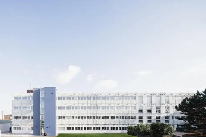 Unternehmensfotografie: Bürogebäude mit Fensterfassade und blauem Treppenhaus vor blauem Himmel.