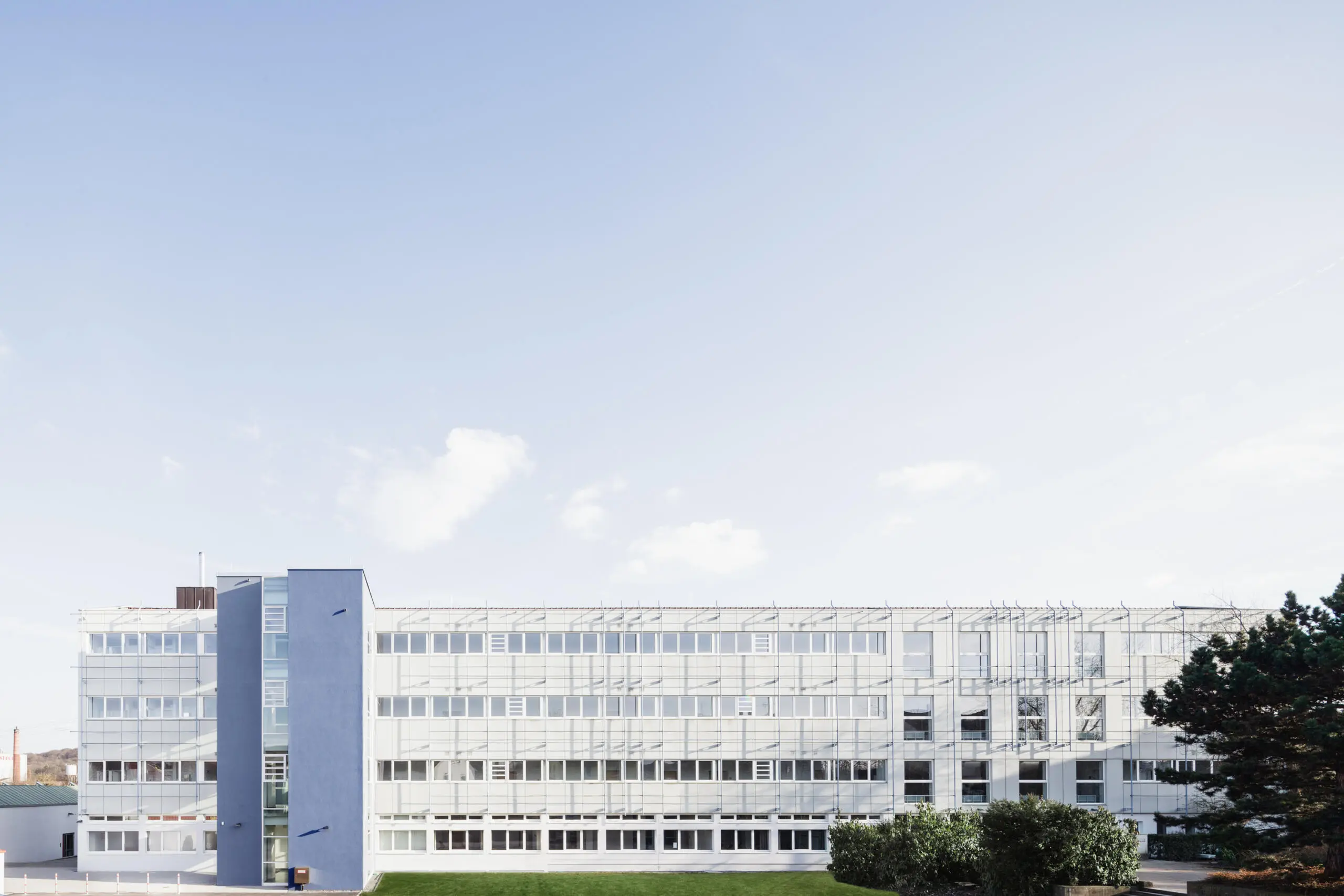 Unternehmensfotografie: Bürogebäude mit Fensterfassade und blauem Treppenhaus vor blauem Himmel.