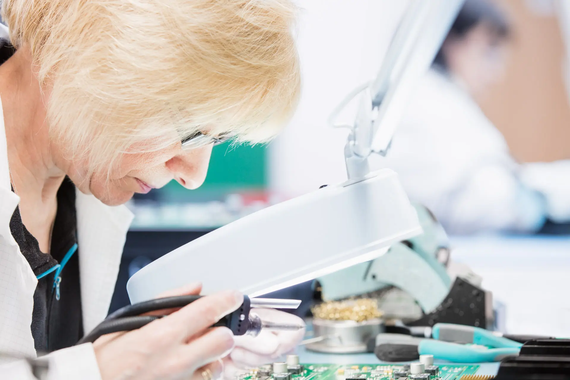 Frau arbeitet an Elektronik mit Lupe: Unternehmensfotografie, Fertigung, Technik.