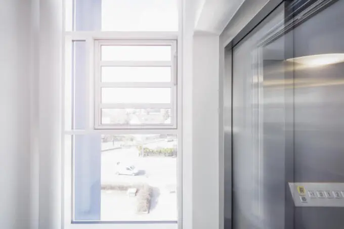 Helle Unternehmensfotografie: Fenster und Aufzug in moderner Büroarchitektur mit Tageslicht.