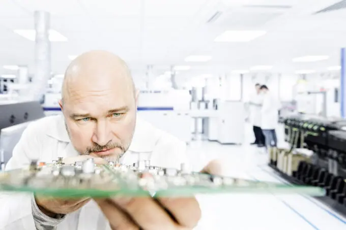 Mann in Reinraum prüft Leiterplatte, Unternehmensfotografie.
