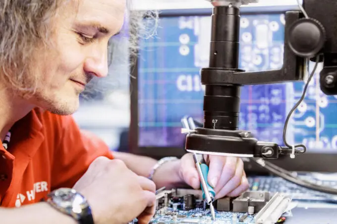 Unternehmensfotografie: Mitarbeiter arbeitet an elektronischer Platine unter dem Mikroskop.
