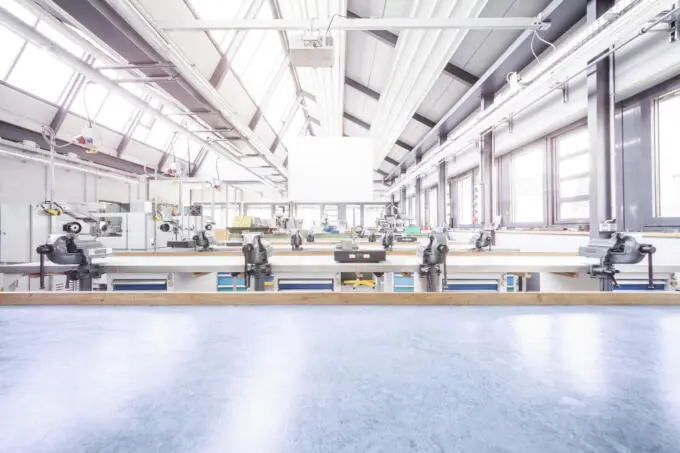 Helle Werkshalle: Arbeitsplätze mit Schraubstöcken. Industriefotografie einer Produktionsstätte.