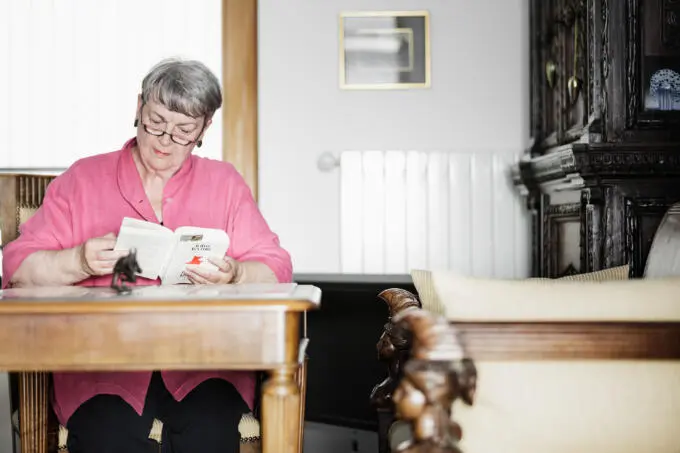 Frau liest Buch am Tisch in einem Raum.