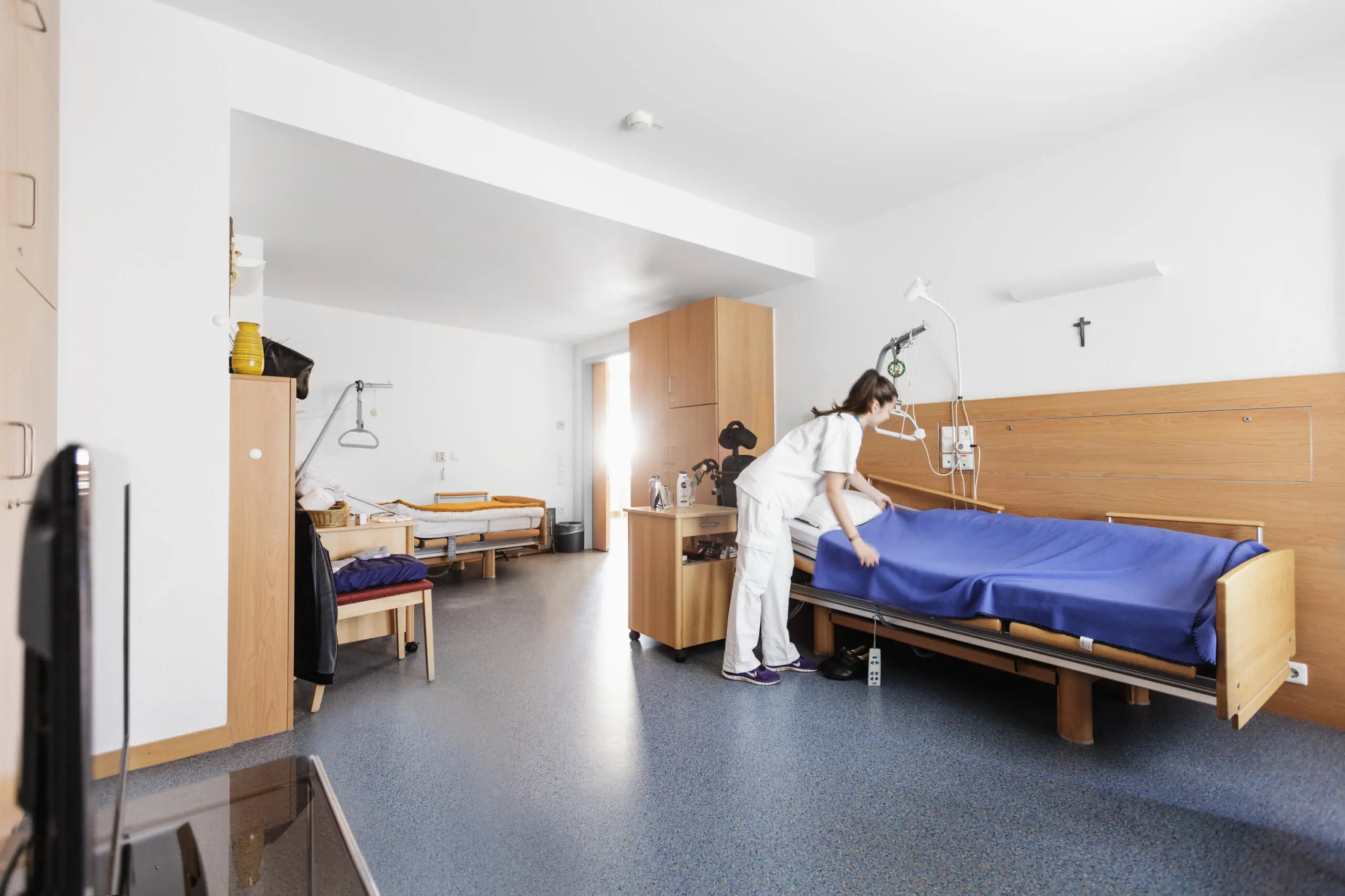 Eine Krankenschwester macht ein Bett in einem hellen Klinikraum.