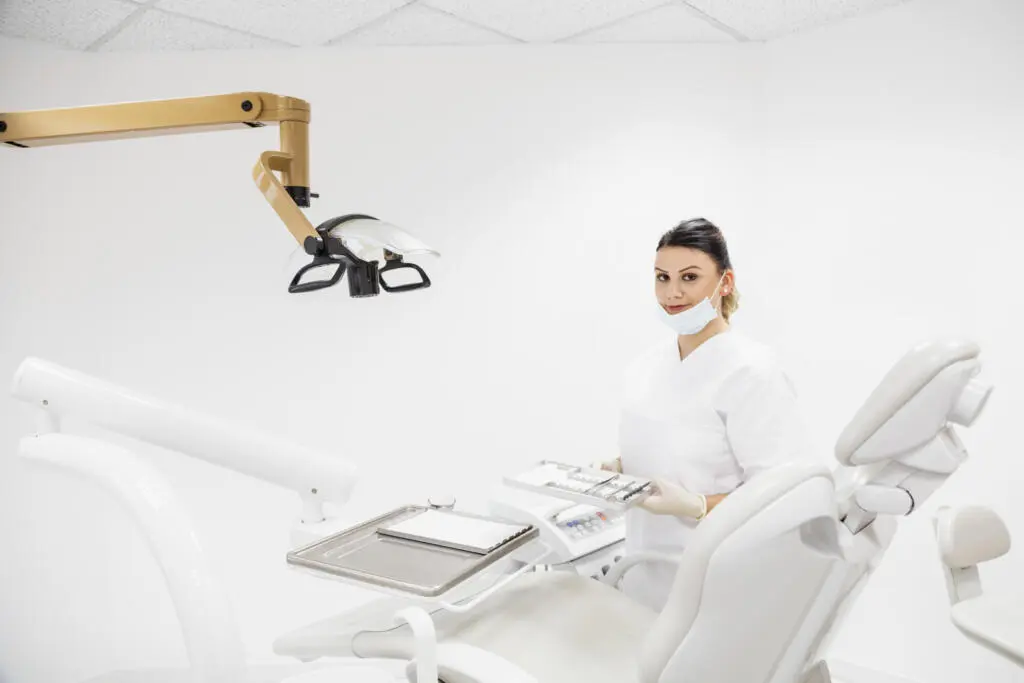 Zahnmedizinische Fachangestellte in weißer Kleidung mit Instrumententablett im hellen Behandlungszimmer einer Zahnarztpraxis
