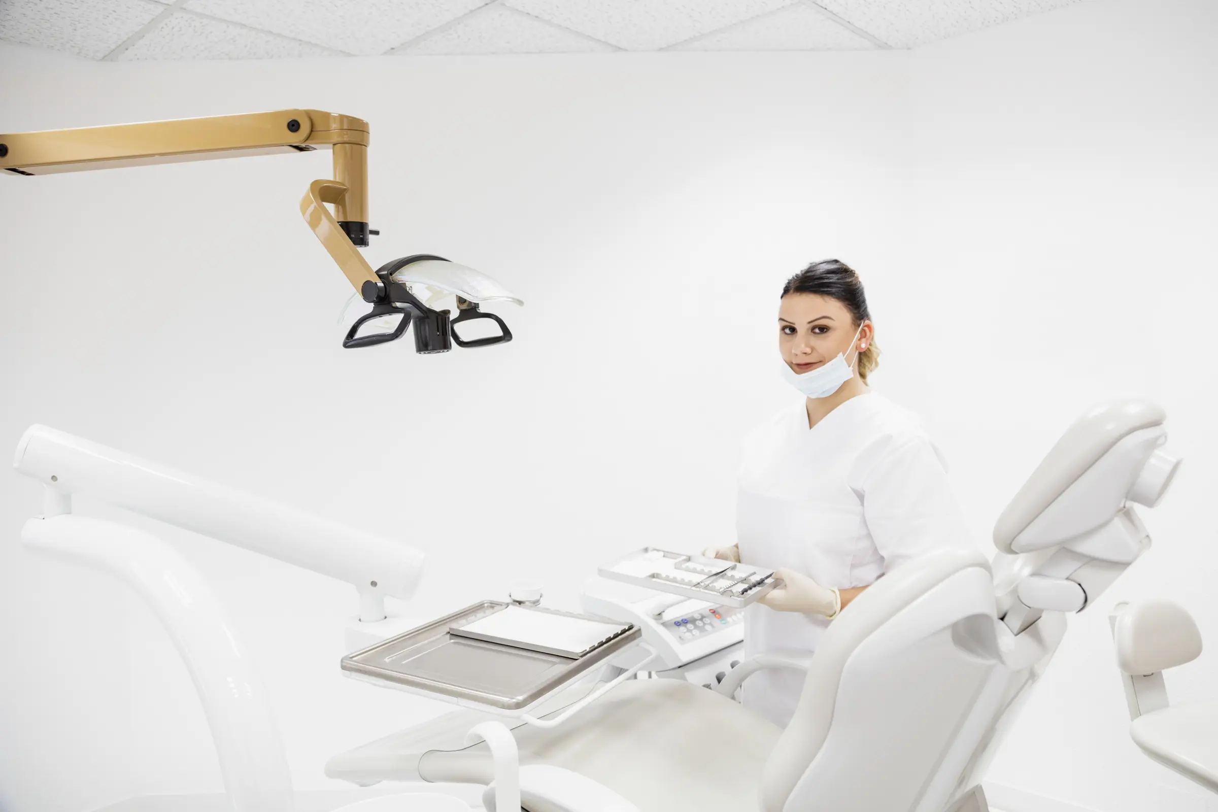 Zahnmedizinische Fachangestellte in weißer Kleidung mit Instrumententablett im hellen Behandlungszimmer einer Zahnarztpraxis