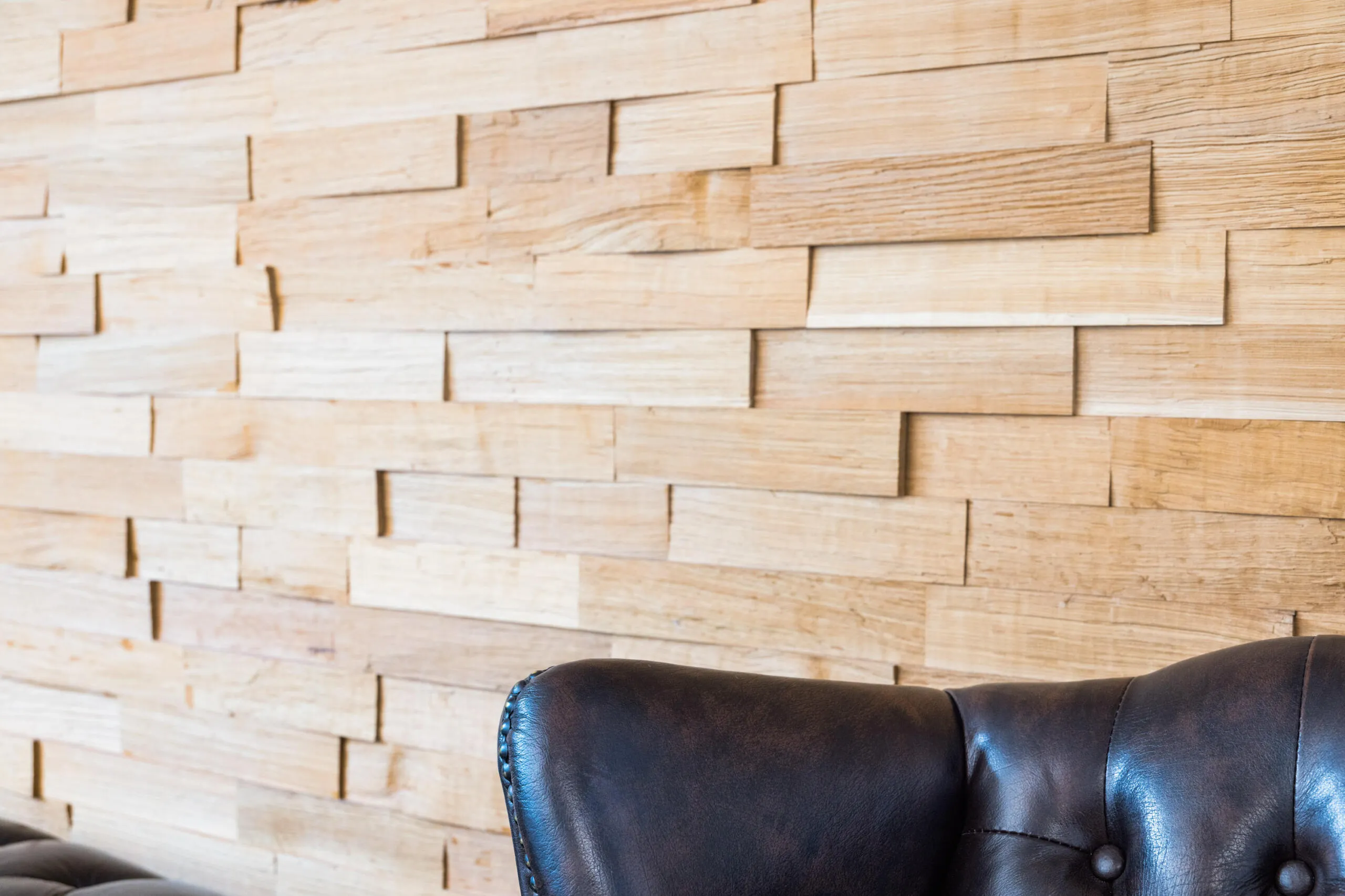 Detailansicht einer hellen Holzwand mit 3D-Struktur und der Rückenlehne eines dunklen Ledersessels