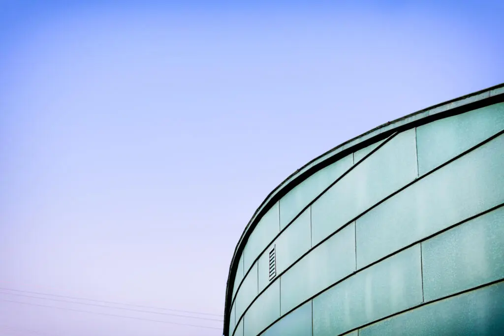 Detailansicht einer geschwungenen Metallfassade eines Umspannwerks vor einem blau-violetten Himmelsverlauf