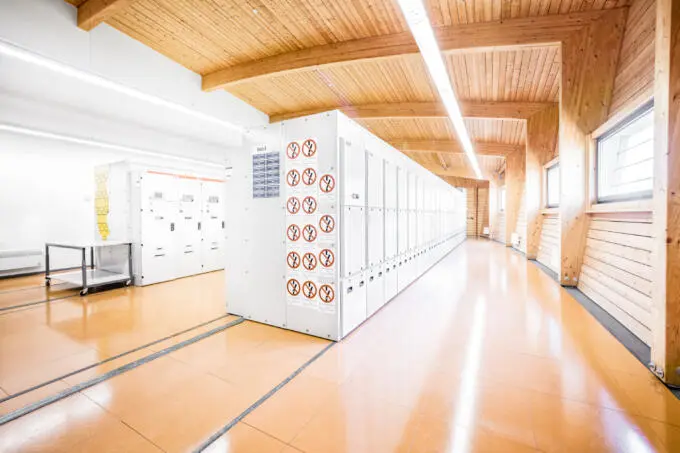 Innenraum einer Schaltanlage mit weißen Schaltschrankreihen, orangefarbenem Boden und Holzdecke