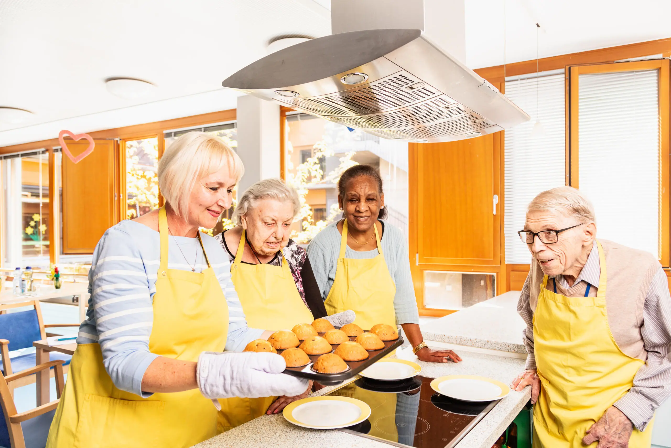 Eine Gruppe älterer Menschen backt zusammen Muffins in einer hellen Küche.