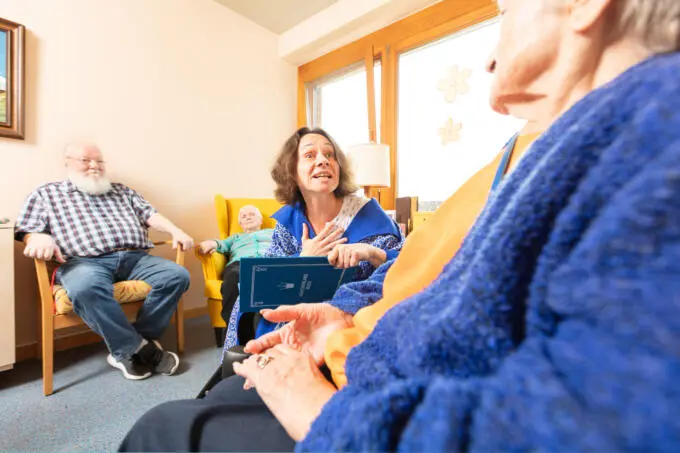 Eine Frau liest Märchenbuch in einer Seniorengruppe vor.