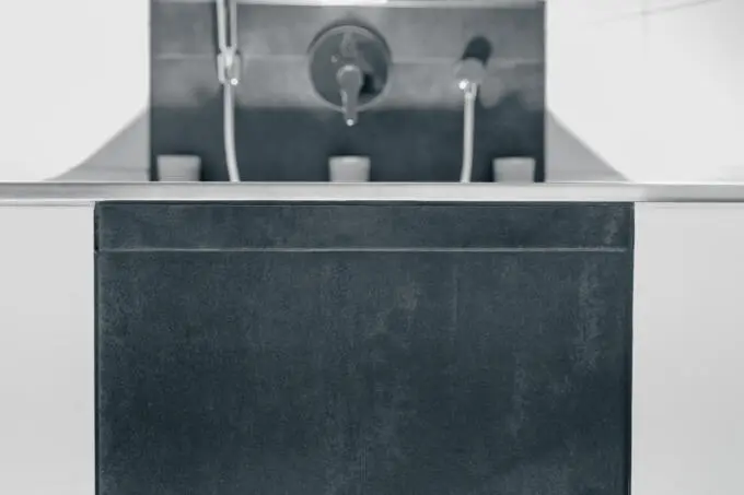 Detailaufnahme einer dunklen Badewannenverkleidung mit Metallkante und unscharfen Armaturen im Hintergrund in Schwarz-Weiß