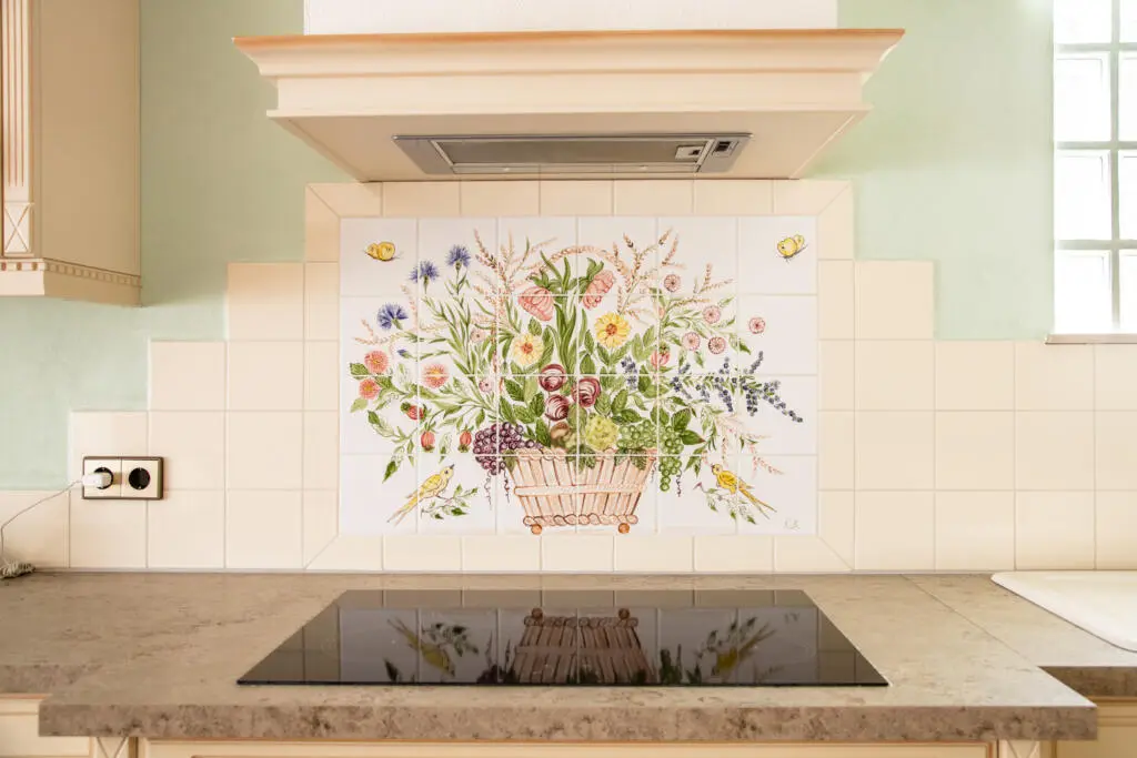 Frontalansicht eines gefliesten Küchenspiegels mit handgemaltem Blumenkorb-Motiv über einem Induktionskochfeld