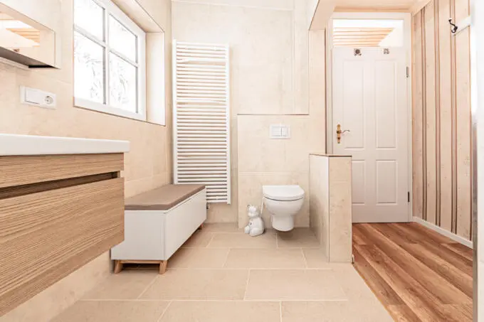 Helles Badezimmer mit beigen großformatigen Fliesen an Wand und Boden, Holz-Waschtisch und weißem Heizkörper