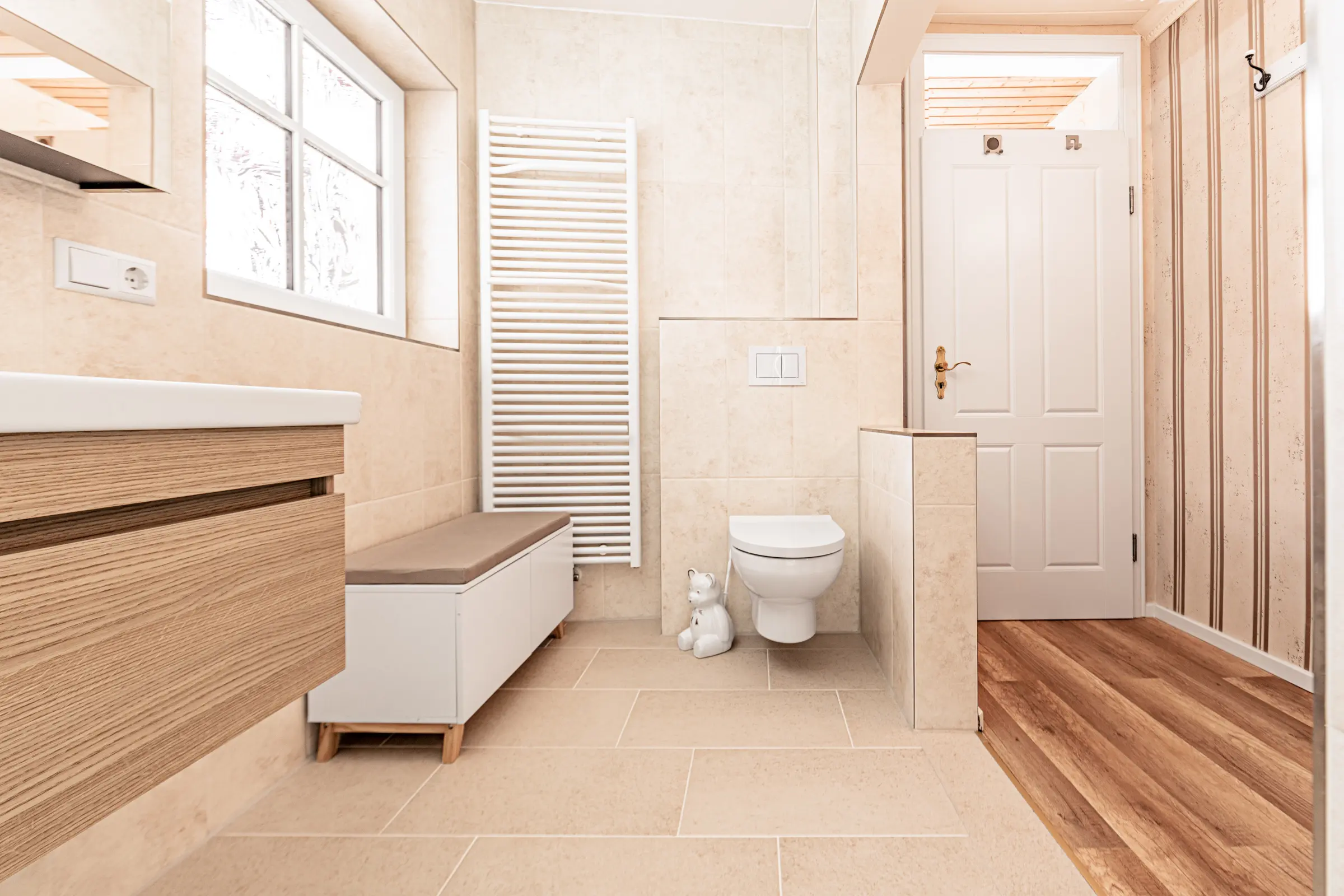 Helles Badezimmer mit beigen großformatigen Fliesen an Wand und Boden, Holz-Waschtisch und weißem Heizkörper