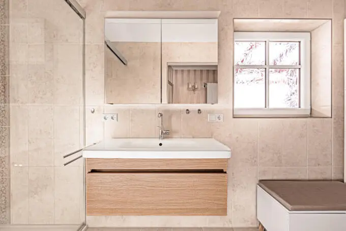 Badezimmer mit beigen Fliesen, Holz-Waschtisch, Spiegelschrank und Fenster
