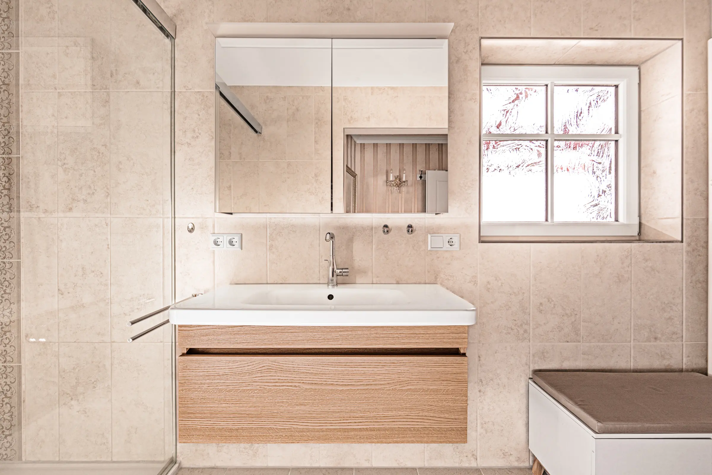 Badezimmer mit beigen Fliesen, Holz-Waschtisch, Spiegelschrank und Fenster
