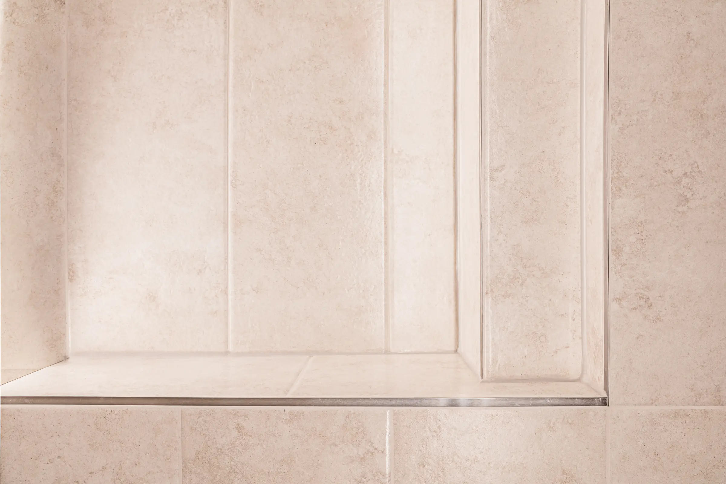 Nahaufnahme einer gefliesten Duschnische mit beigen Fliesen in Steinoptik und Metallkante