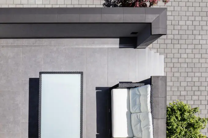 Draufsicht auf eine moderne Terrasse mit grauen Großformatfliesen, weißen Loungemöbeln und angrenzendem Pflastersteinweg