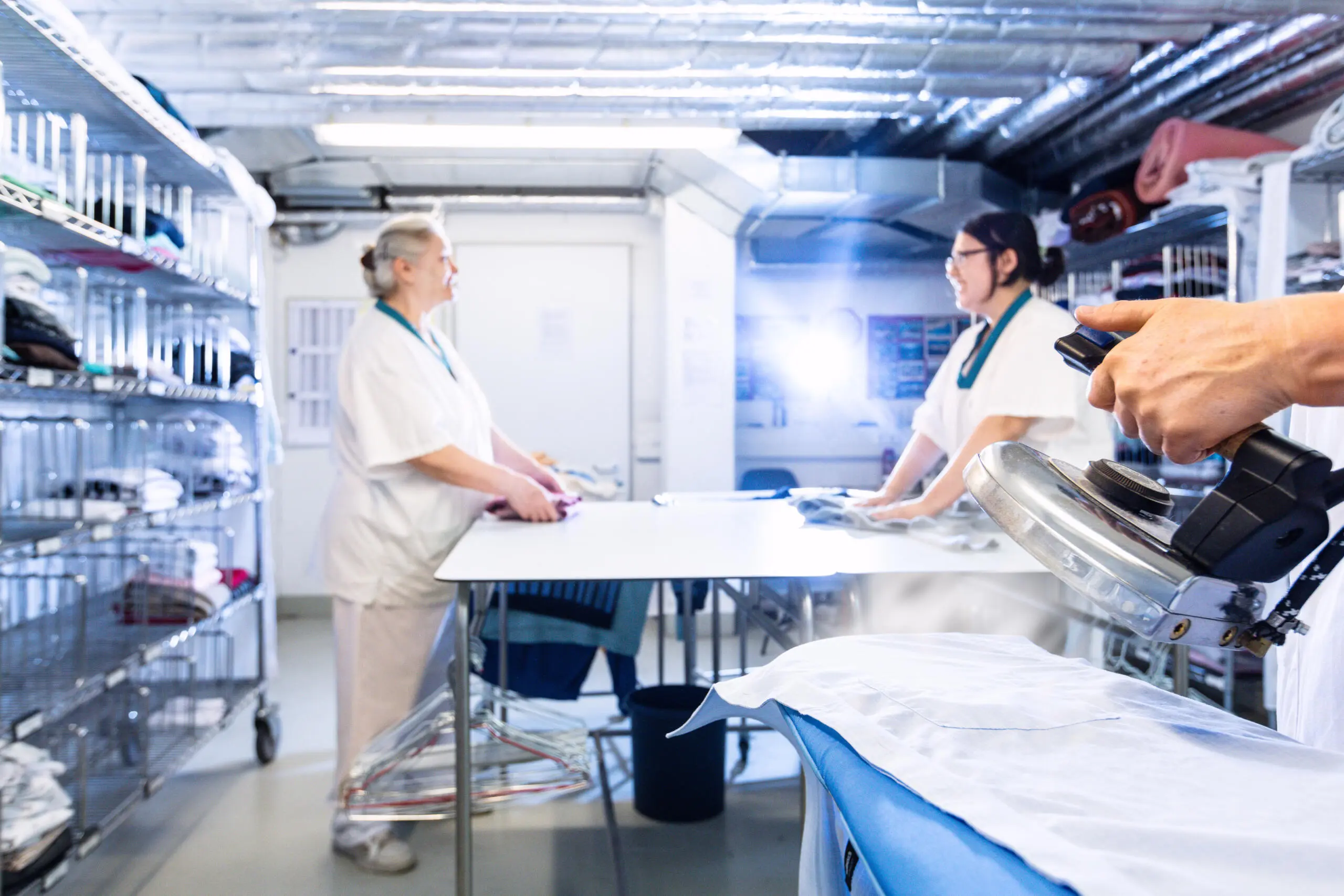 Professionelle Textilreinigung mit Bügeleisen und Personal in heller Umgebung.