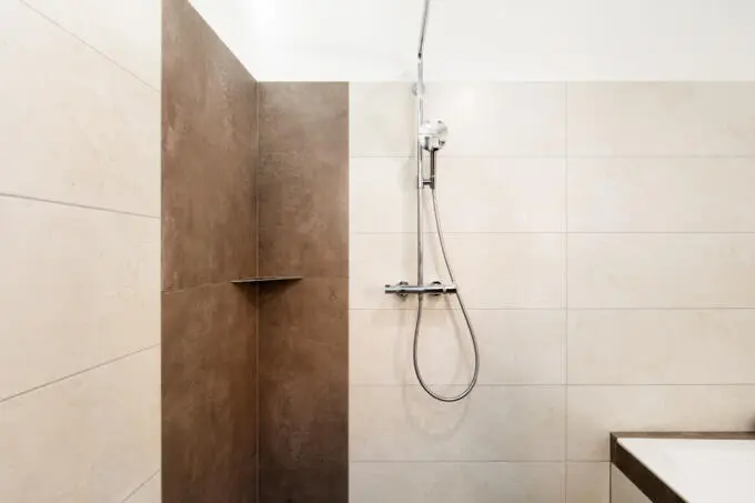 Duschbereich mit hellbeigen Fliesen und dunkelbraunem Akzentstreifen sowie verchromter Armatur