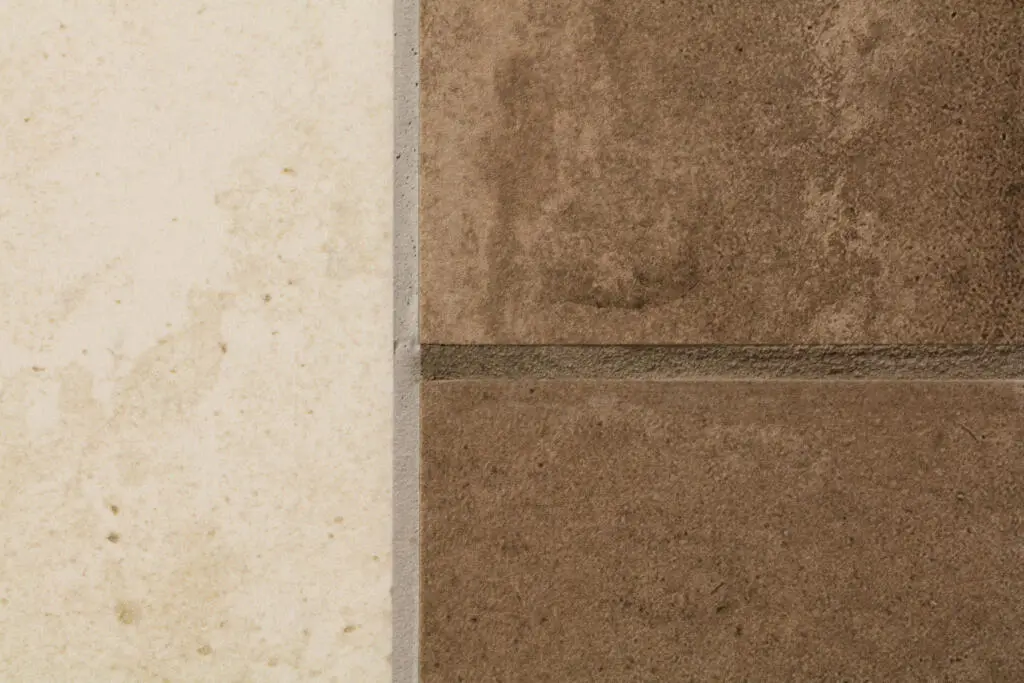 Nahaufnahme eines Übergangs zwischen einer hellen beigen und zwei dunklen braunen Fliesen mit grauen Fugen in Steinoptik