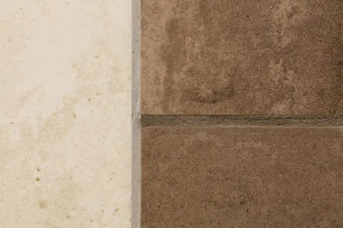 Nahaufnahme eines Übergangs zwischen einer hellen beigen und zwei dunklen braunen Fliesen mit grauen Fugen in Steinoptik