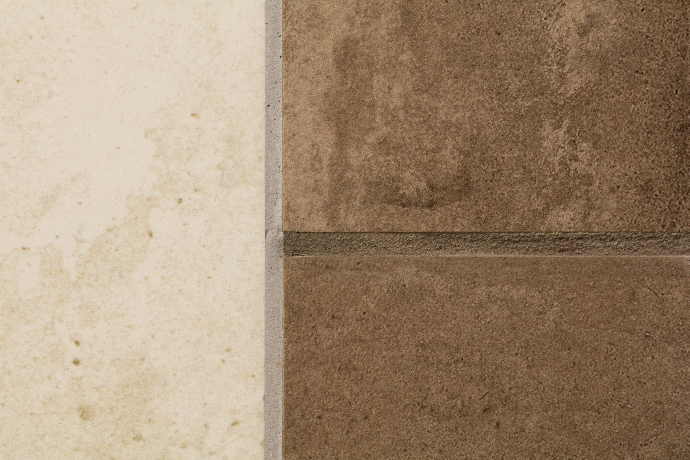 Nahaufnahme eines Übergangs zwischen einer hellen beigen und zwei dunklen braunen Fliesen mit grauen Fugen in Steinoptik