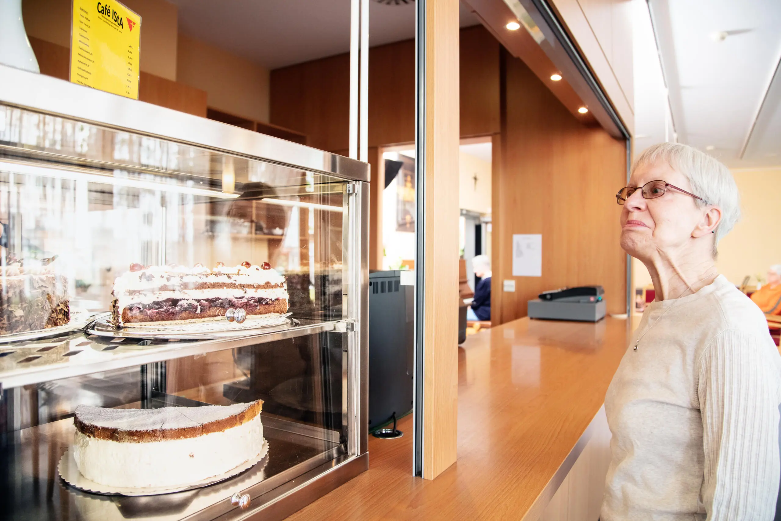 Ältere Dame betrachtet Kuchen in einem Café.