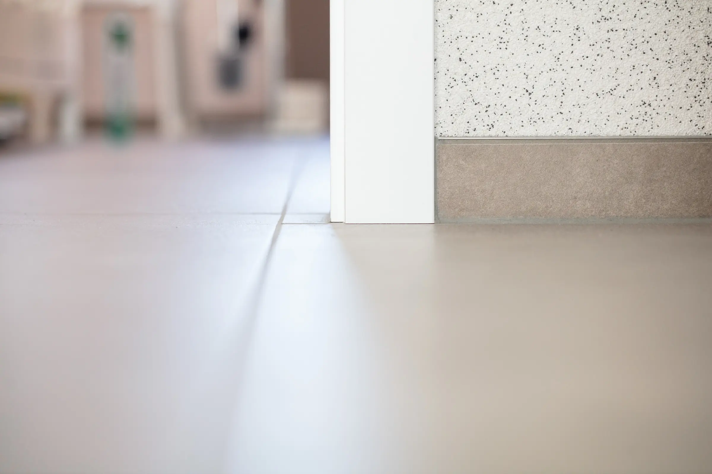 Nahaufnahme von Bodenfliesen mit Anschluss an weißen Türrahmen und Sockelleiste
