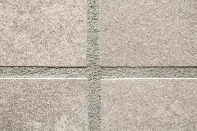 Detailansicht eines Fugenkreuzes zwischen vier beigen Fliesen mit grauer Fugenmasse