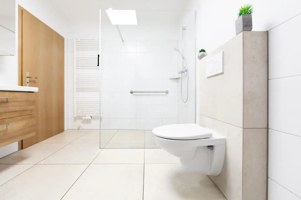 Modernes barrierefreies Badezimmer mit beigen Bodenfliesen, weißen Wandfliesen, begehbarer Glasdusche und Wand-WC