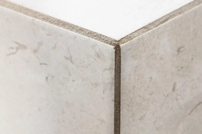 Nahaufnahme einer gefliesten Außenecke mit beigen Fliesen und grauer Fugenmasse im Detail