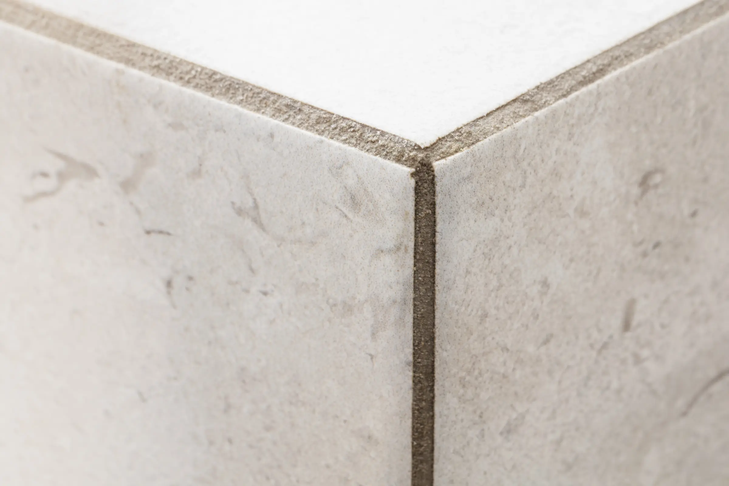 Nahaufnahme einer gefliesten Außenecke mit beigen Fliesen und grauer Fugenmasse im Detail