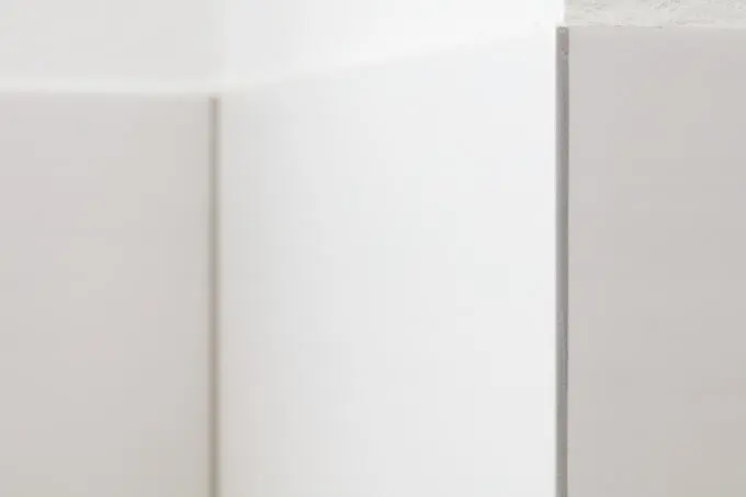Detailansicht einer vertikalen Fliesenkante mit grauem Abschlussprofil an einer weißen Wand