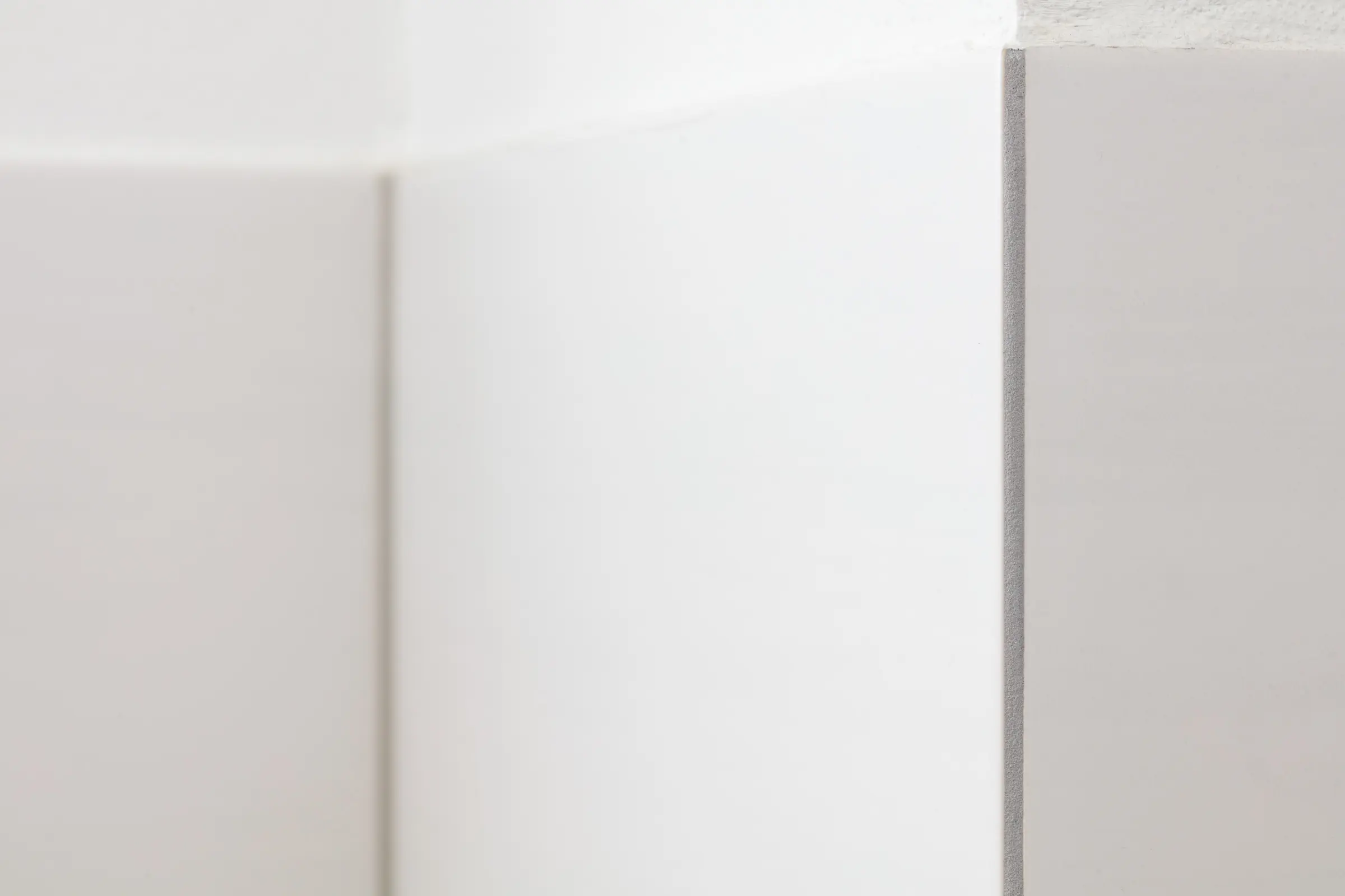 Detailansicht einer vertikalen Fliesenkante mit grauem Abschlussprofil an einer weißen Wand