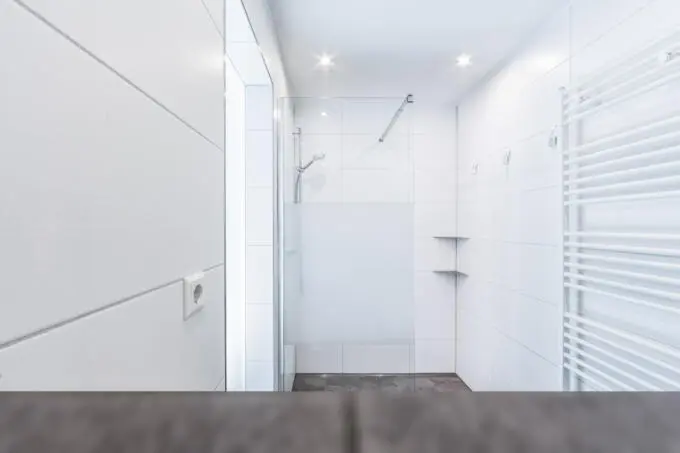 Modernes Badezimmer mit weißen Wandfliesen, Glasdusche mit Sichtschutz und Handtuchheizkörper