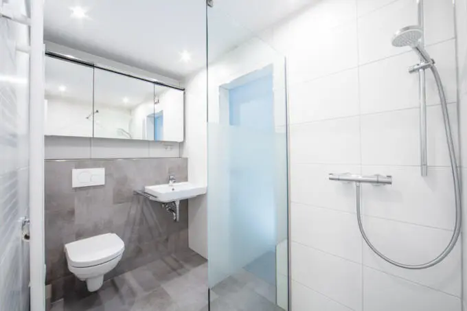 Modernes Badezimmer mit grauen und weißen Fliesen, Glasdusche, WC und Waschbecken