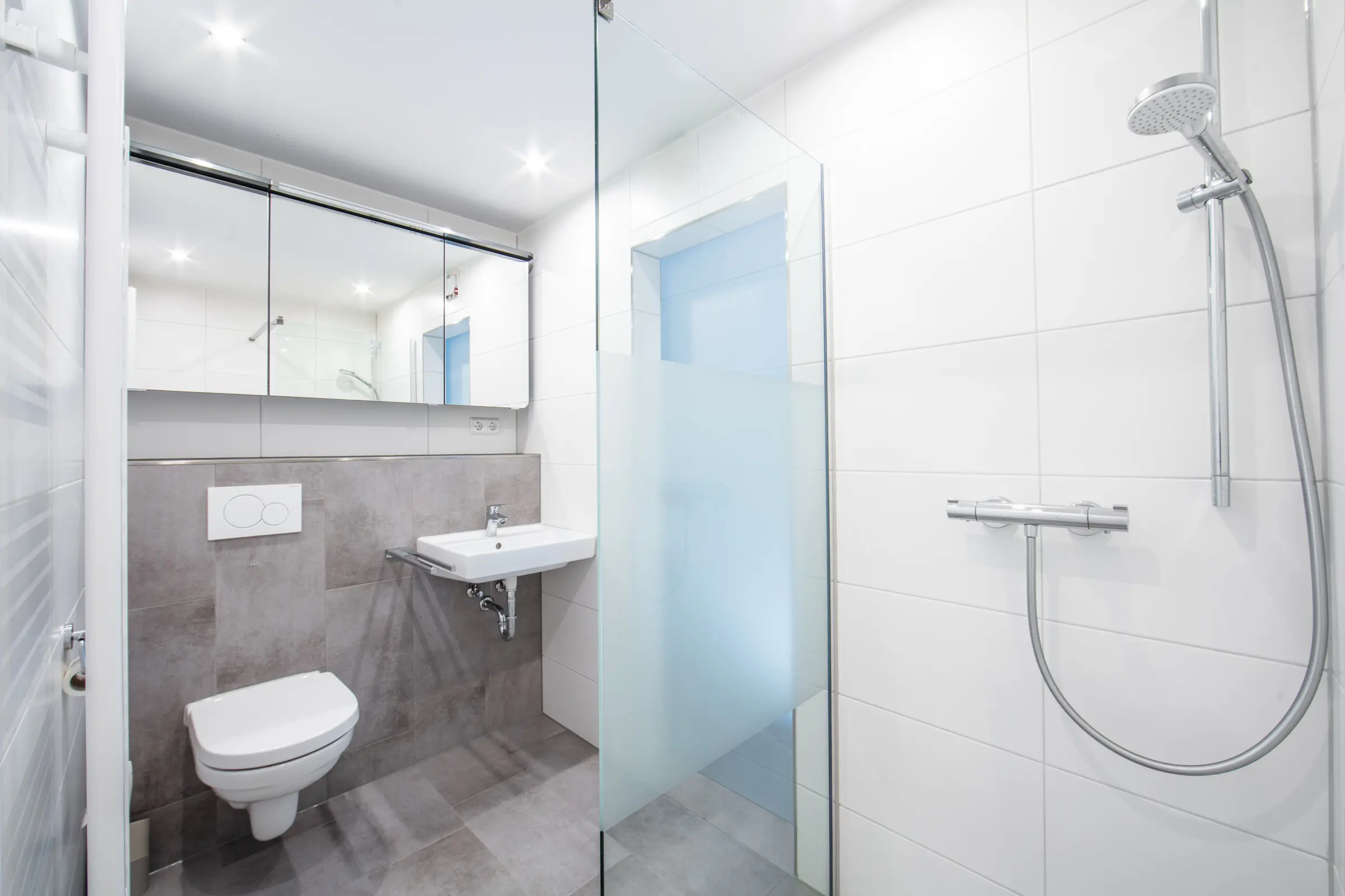 Modernes Badezimmer mit grauen und weißen Fliesen, Glasdusche, WC und Waschbecken