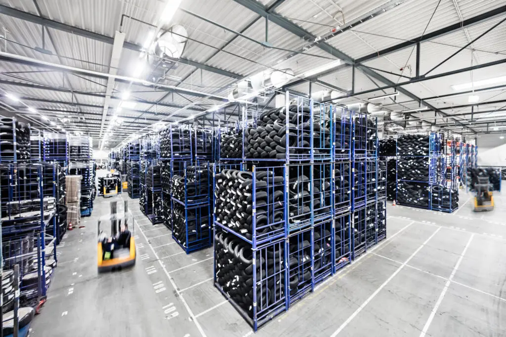 Weitwinkelaufnahme einer großen Lagerhalle mit hohen Regalen voller Autoreifen und einem fahrenden Gabelstapler mit Bewegungsunschärfe