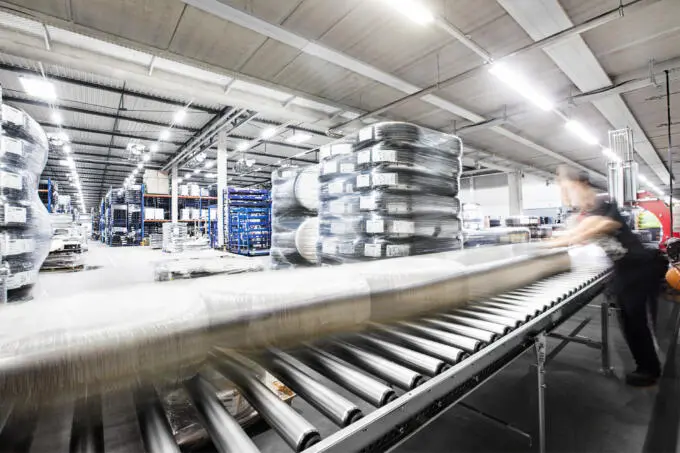 Rollenförderband in einer Lagerhalle mit bewegungsunscharfen verpackten Reifen und einem Arbeiter