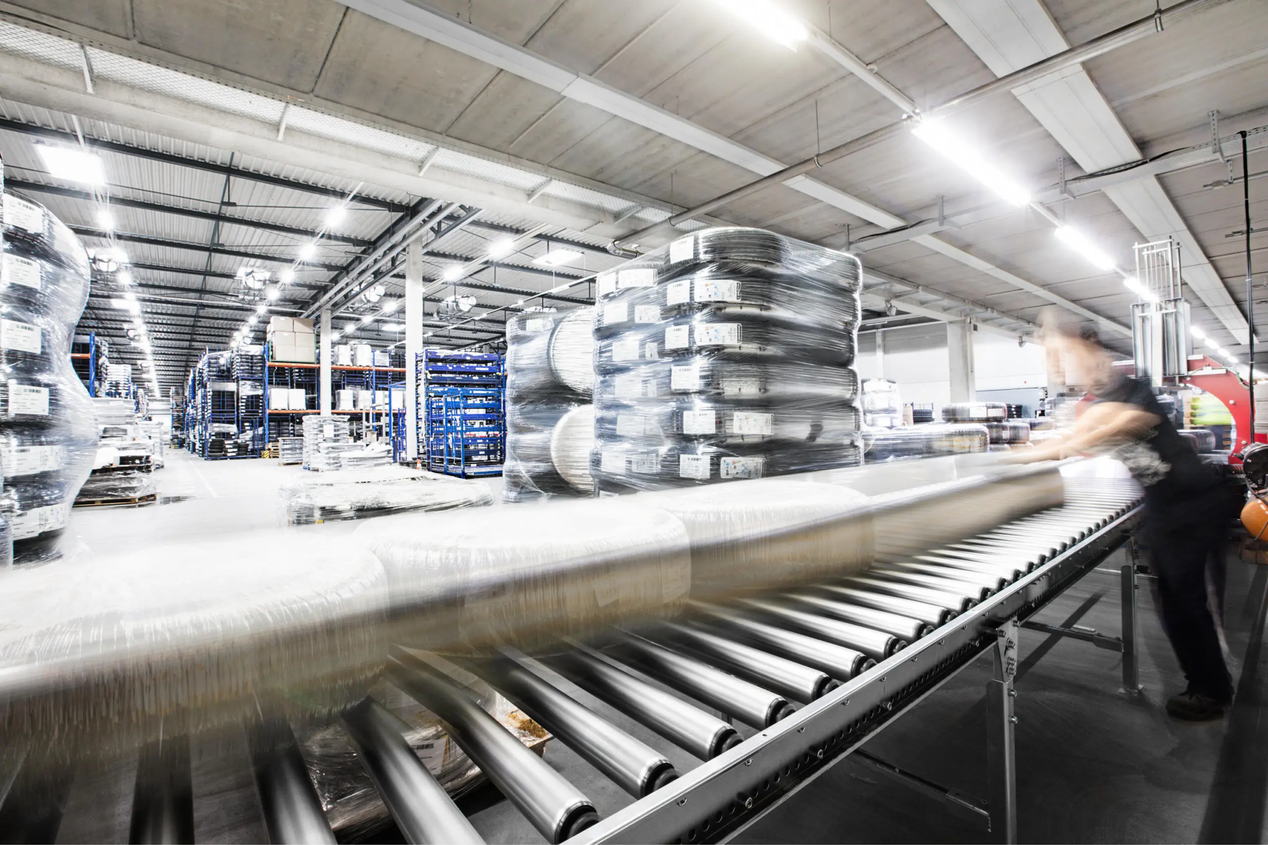 Rollenförderband in einer Lagerhalle mit bewegungsunscharfen verpackten Reifen und einem Arbeiter