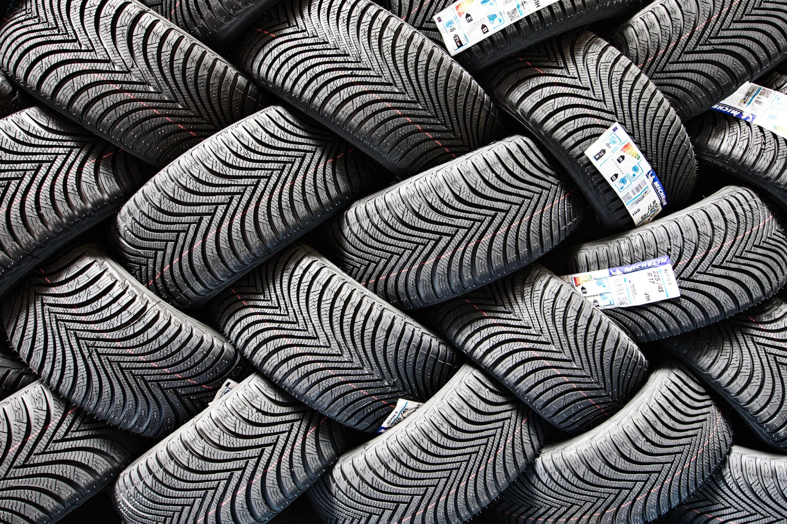 Detailansicht gestapelter neuer Winterreifen mit V-Profil und Etiketten im Lager