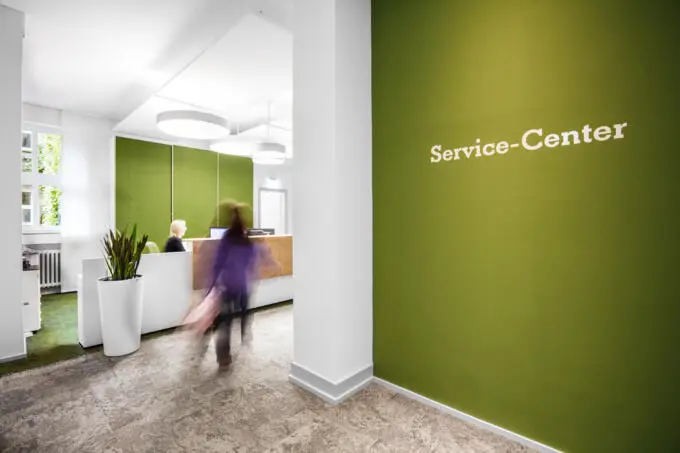 Heller Empfangsbereich eines Service-Centers mit grüner Wand und bewegungsunscharfer Person