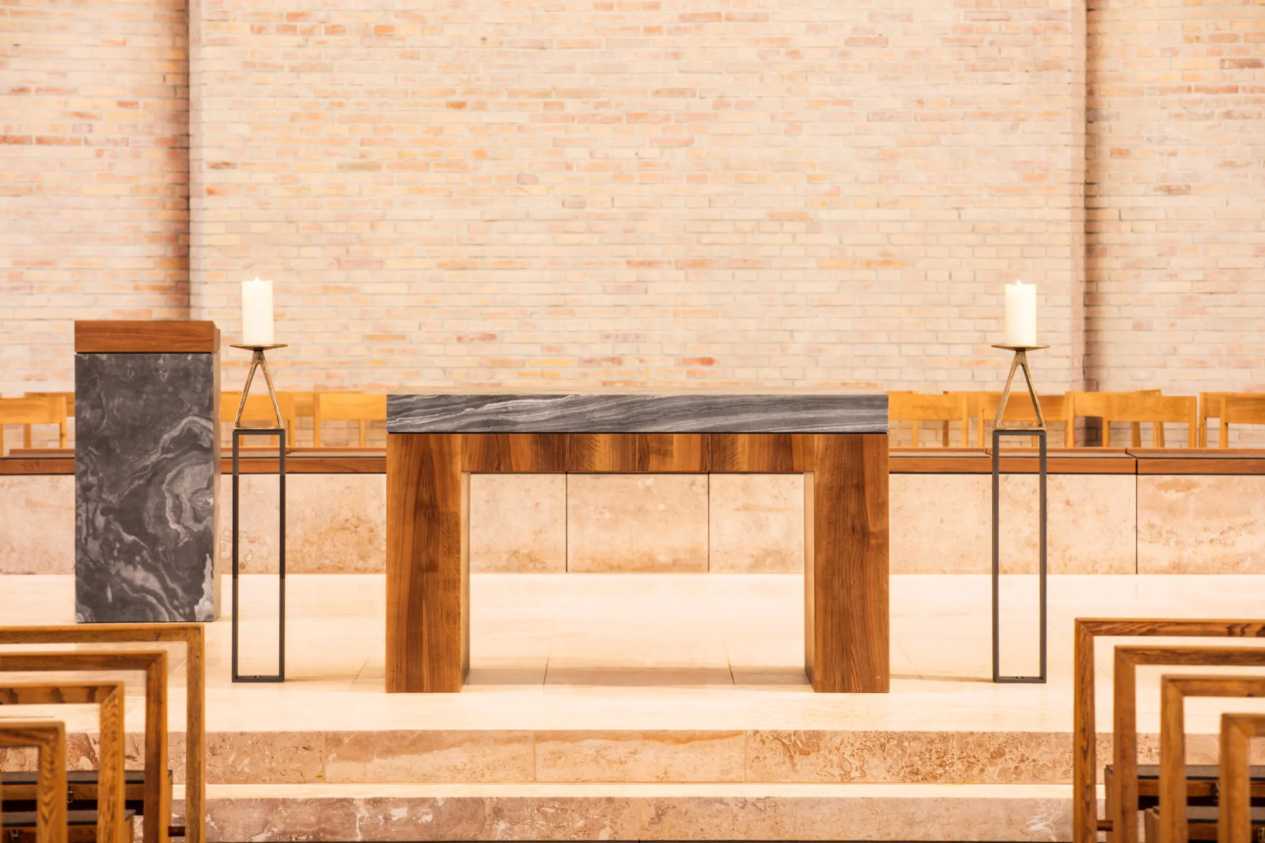 Moderner Altar aus Holz und Stein mit Ambo und Kerzenständern vor heller Ziegelwand in einer Kirche