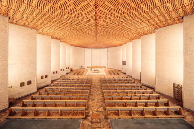 Symmetrischer Innenraum einer modernen Kirche mit hellen Backsteinwänden und aufwendiger Holzlamellendecke