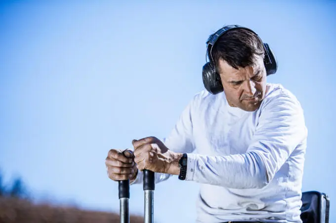 Bauarbeiter mit Kapselgehörschutz bedient die Steuerhebel einer Baumaschine vor blauem Himmel