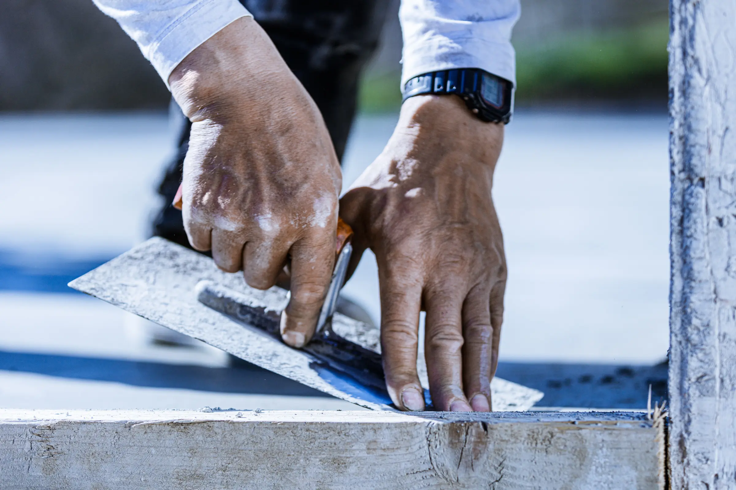 Nahaufnahme der Hände eines Handwerkers beim Glätten von Beton mit einer Kelle an einer Holzkante
